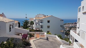 Ein Küstenwohngebiet mit weißen Gebäuden, einem gepflasterten Innenhof und Blick aufs Meer.