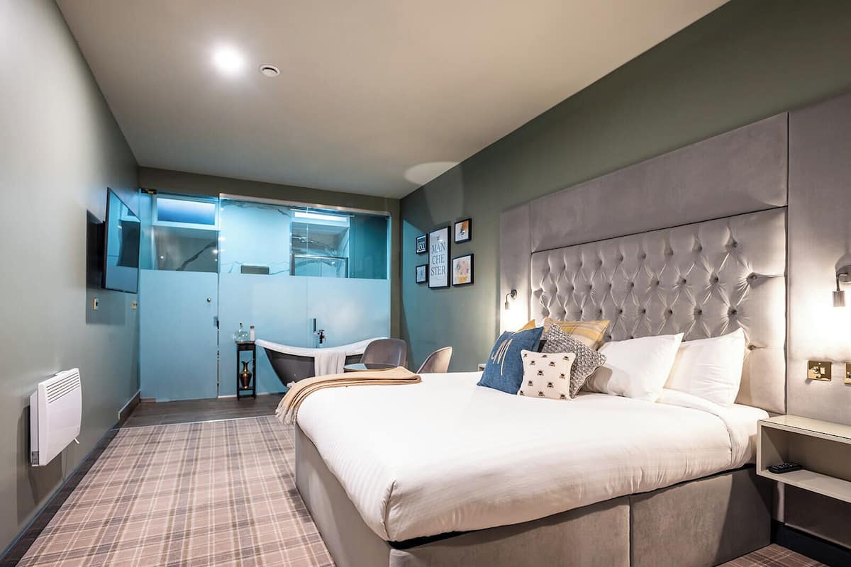 A modern hotel room with a large bed, a vanity with a mirror, and a small desk.