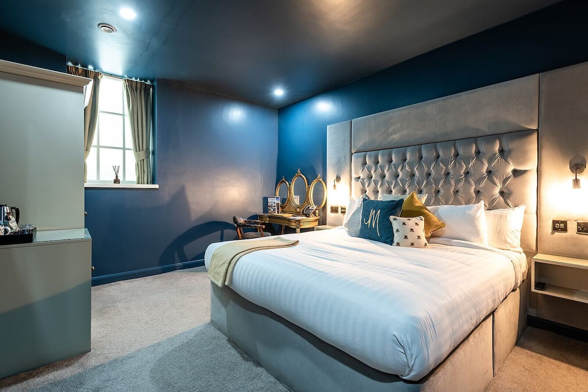 A modern bedroom with a large bed, a vanity with mirrors, and a desk.