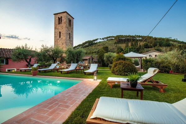 Relax by the serene pool surrounded by lush greenery and a historic stone tower.