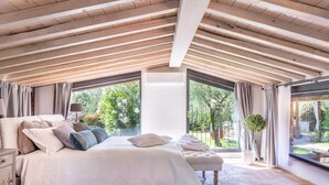 A bedroom with a large bed, a bench, and a view of the garden through a glass door.
