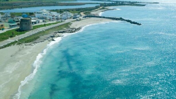 An aerial view of a coastal area with a beach, a pier, and buildings including a tower-like structure. - LAST MINUTE Torre Mozza - Apartment on the sea 21 (Torre Mozza, Lecce)