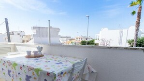 A balcony with a table covered in a floral tablecloth, white chairs, and a small table with a pitcher and cups. - LAST MINUTE Torre Mozza - Apartment on the sea 21 (Torre Mozza, Lecce)