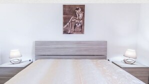 A bedroom with a bed, two bedside tables, and a wall-mounted painting. - LAST MINUTE Torre Mozza - Apartment on the sea 21 (Torre Mozza, Lecce)