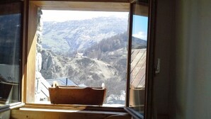 A room with a wooden bench and a window overlooking a mountainous landscape.