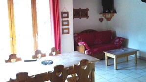 A dining area with a wooden table and chairs, a red sofa, and a small table with a book.