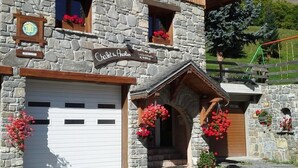 A stone building with a sign reading "Chalet des Anciens." It features a white garage door, stone walls, and wooden beams.