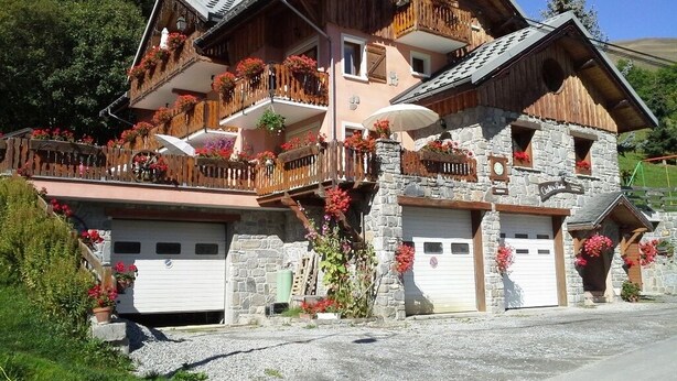 A two-story chalet with a stone facade, wooden balconies, and flower boxes.
