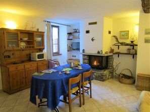 A cozy dining area with a table set for two, a stone fireplace, wooden cabinets, and a television.