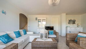 A living room with a white sofa, wicker furniture, a television, and a staircase leading to a balcony.