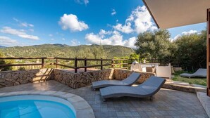 A pool area with lounge chairs and a stone wall, overlooking a mountainous landscape.