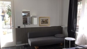 A modern living room with a grey sofa, a small round table, a floor lamp, and a framed picture on the wall.