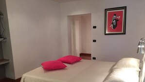 A bedroom with a bed, two pillows, a nightstand, a lamp, and a framed picture on the wall.