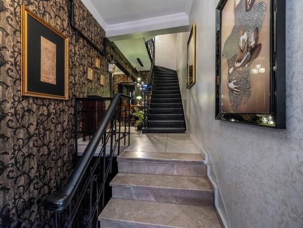 A staircase with a black railing, patterned wallpaper, and framed pictures on the walls.