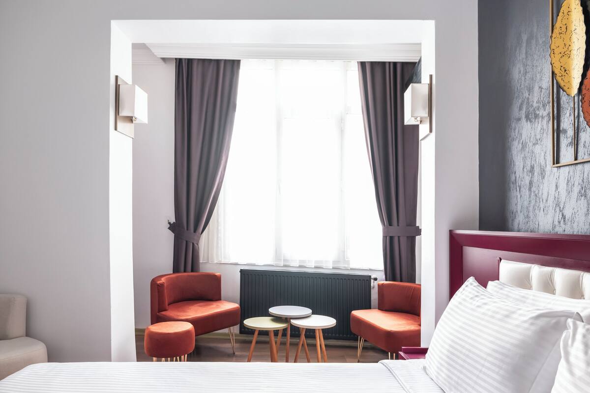 A hotel room with a bed, two armchairs, a small table, and a radiator.