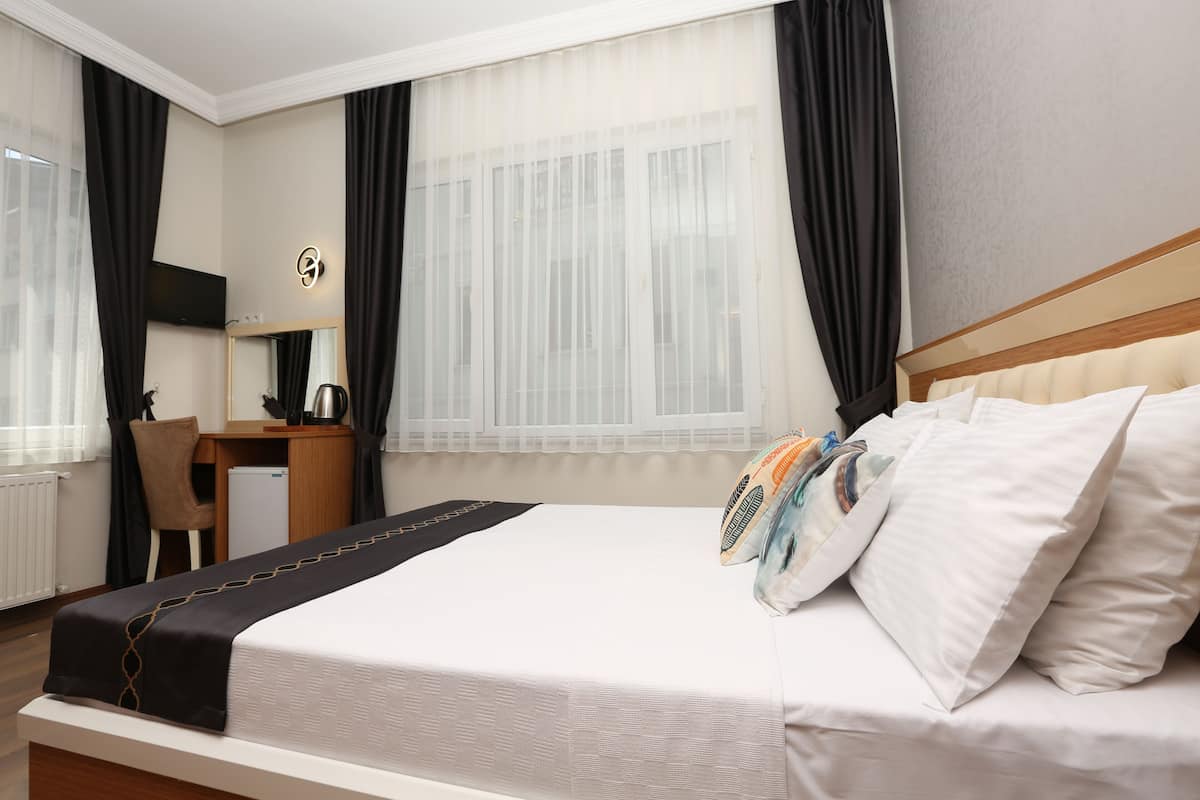 A hotel room with a bed, a desk, a chair, a television, and a window with curtains.