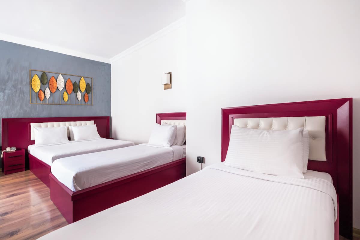 A hotel room with two beds, a red accent wall, and a decorative leaf art piece.