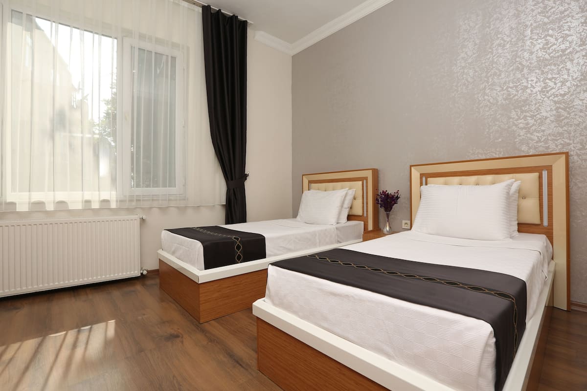 A hotel room with two beds, a radiator, a window with curtains, and a patterned wall.