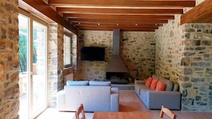 Interior rústic de pedra amb sostre de fusta, una llar de pedra i un saló de sofàs.