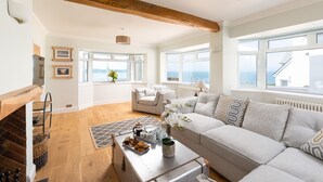 A spacious living room with a large sofa, a coffee table with pastries, and a view of the sea through large windows. - 5 bedroom, pet friendly holiday home in  Woolacombe with private hot tub and stunning sea views (Woolacombe)