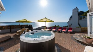 A hot tub with a view of the sea, outdoor seating with umbrellas, and a brick patio. - 5 bedroom, pet friendly holiday home in  Woolacombe with private hot tub and stunning sea views (Woolacombe)