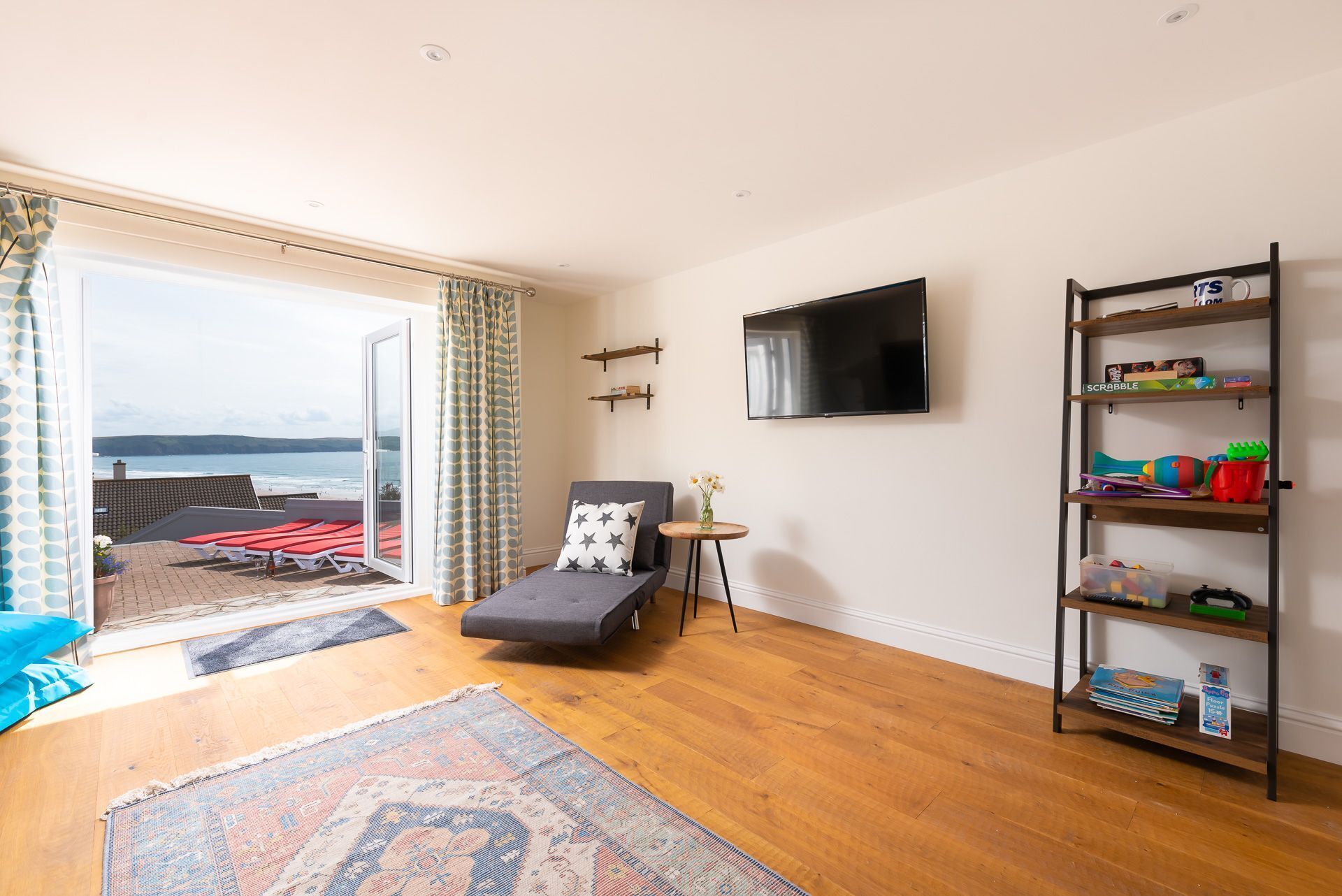 A living room with a sofa, a TV, a bookshelf, and a view of the sea.