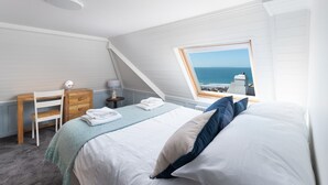A bedroom with a bed, a desk, a chair, and a view of the sea through a window. - 5 bedroom, pet friendly holiday home in  Woolacombe with private hot tub and stunning sea views (Woolacombe)