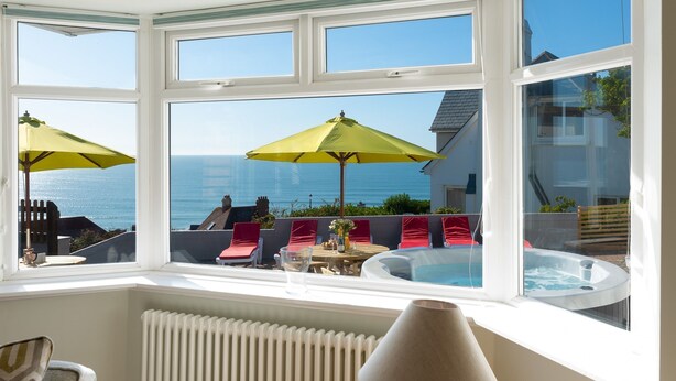 A bay window with a view of the sea, a hot tub, and outdoor seating with umbrellas. - 5 bedroom, pet friendly holiday home in  Woolacombe with private hot tub and stunning sea views (Woolacombe)