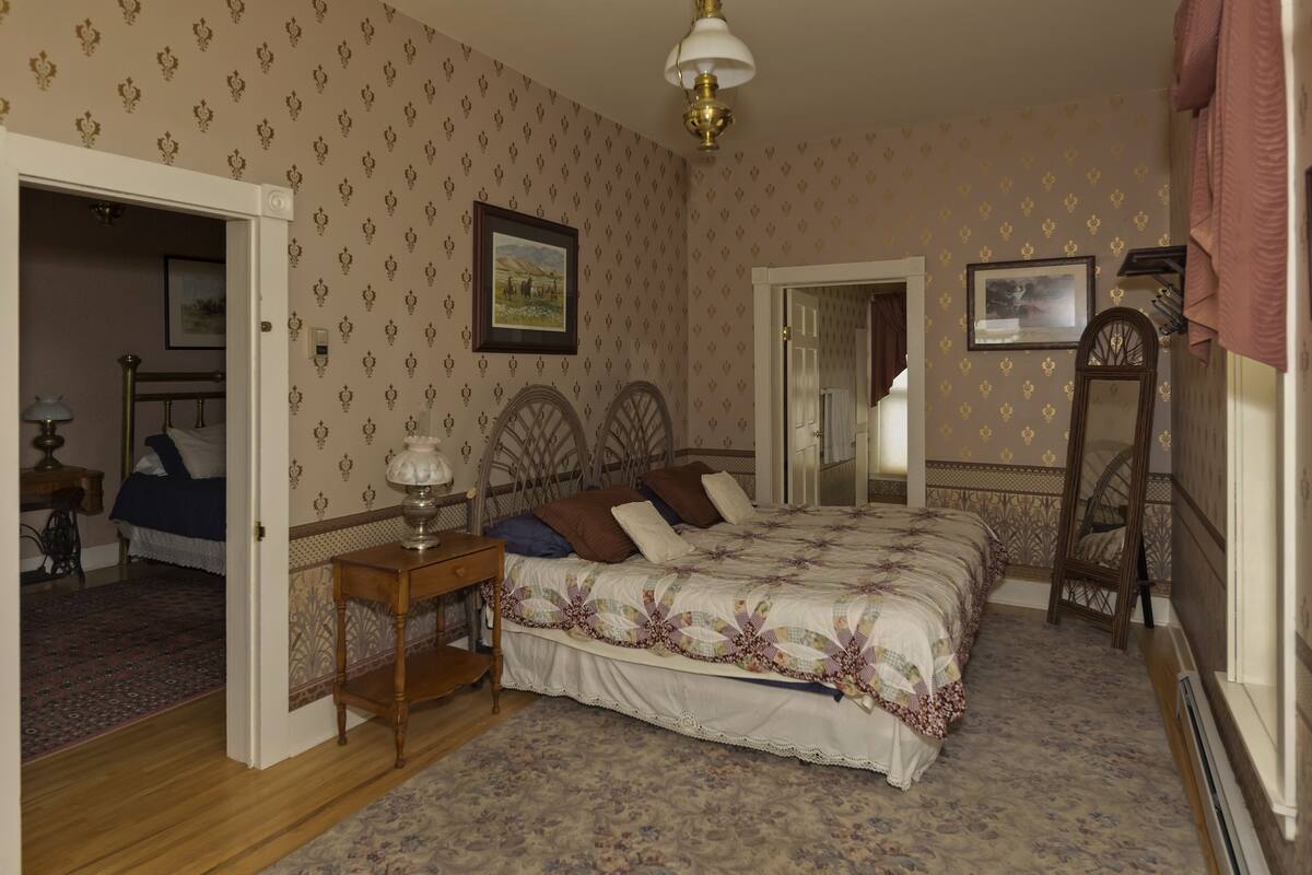 A bedroom with a large bed, a wooden nightstand, a chair, and a door leading to another room.