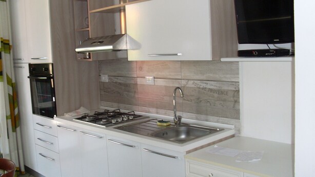 Una cocina moderna con gabinetes blancos, horno empotrado, estufa a gas y pileta de acero inoxidable.