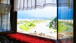 A room with a large window overlooking a cityscape, a red rug, and a view of a river and mountains. - Guva Mangalem (Berat)