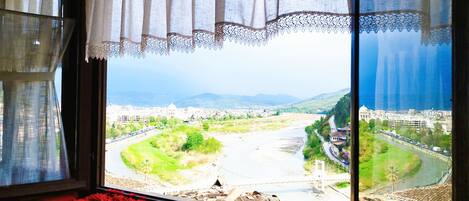A room with a large window overlooking a cityscape, a red rug, and a view of a river and mountains.