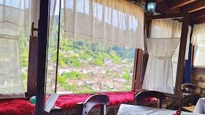 A room with a view of a hillside village, stone walls, a red chair, a table with a checkered tablecloth, and a lantern. - Guva Mangalem (Berat)