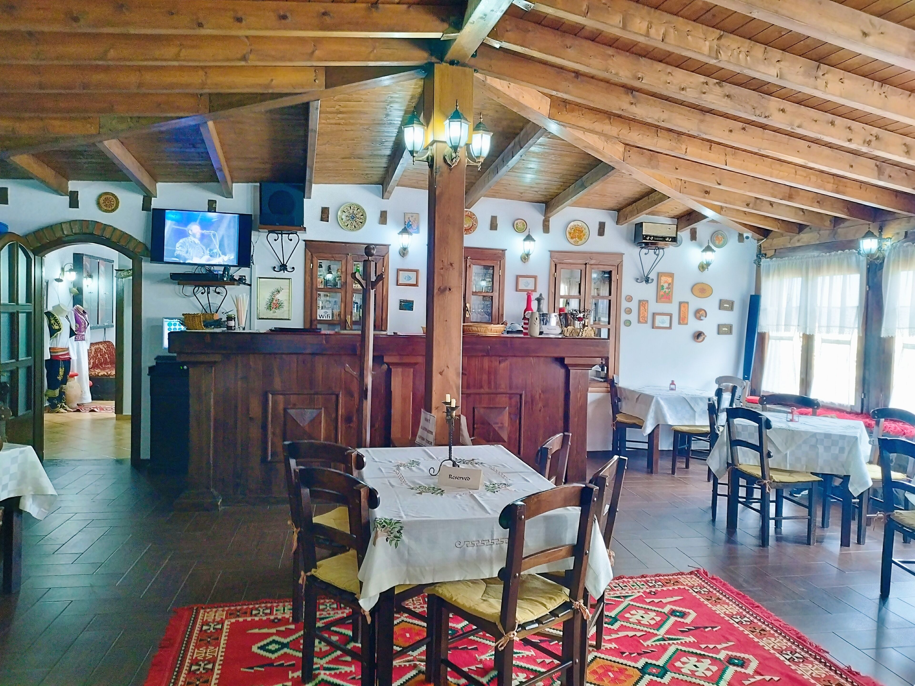 Un restaurante con vigas de madera, una zona de bar y mesas con sillas.