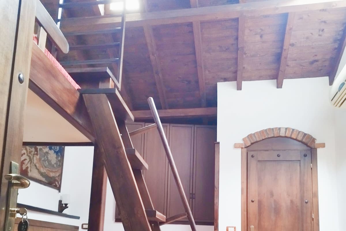 A room with a wooden bunk bed, a ladder, a door, and a tiled floor.