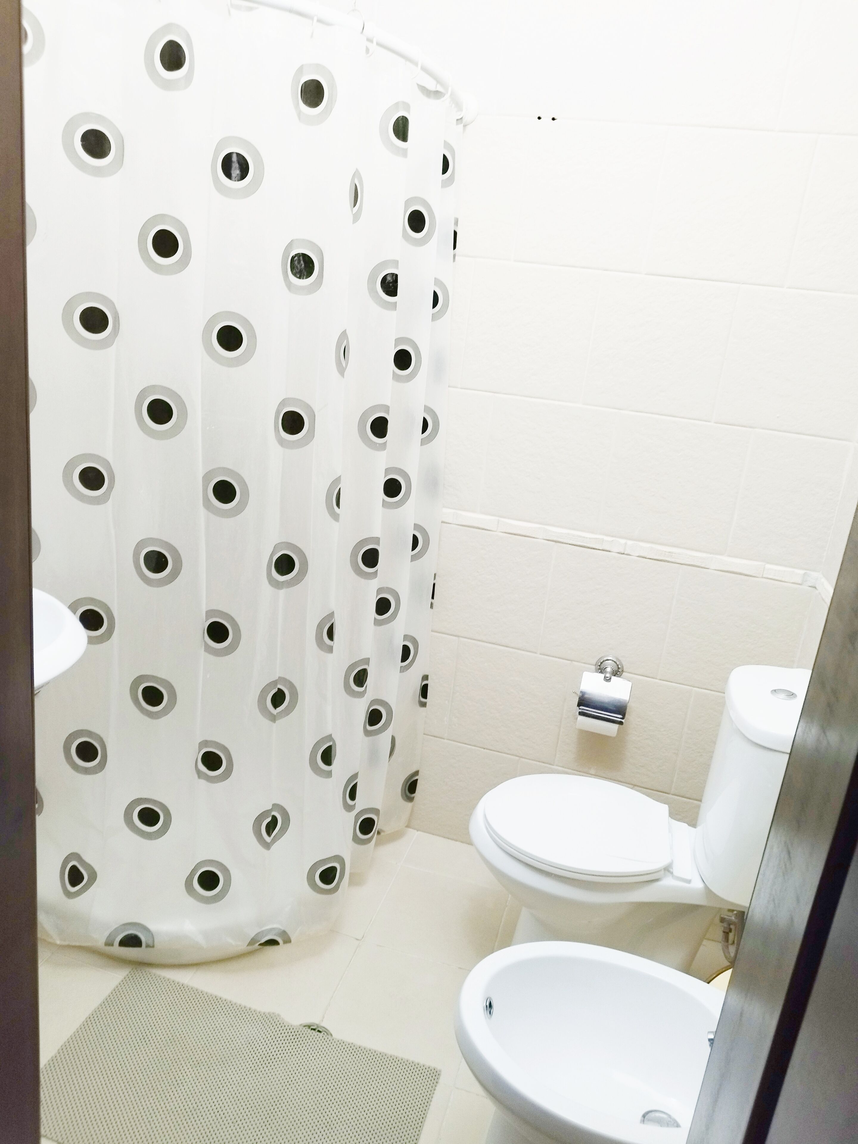 A bathroom with a toilet, bidet, and a shower curtain with circular patterns.