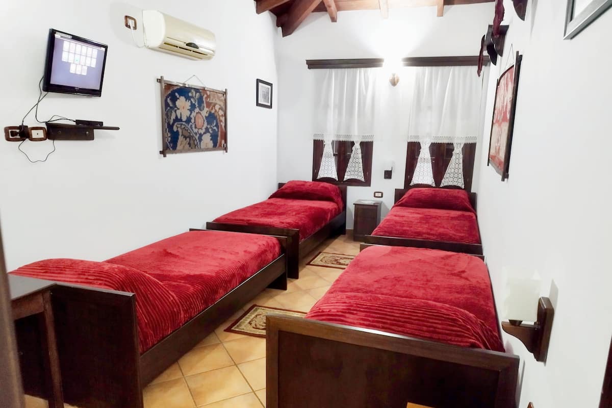 A room with four single beds, a wall-mounted air conditioner, a television, and a patterned rug.