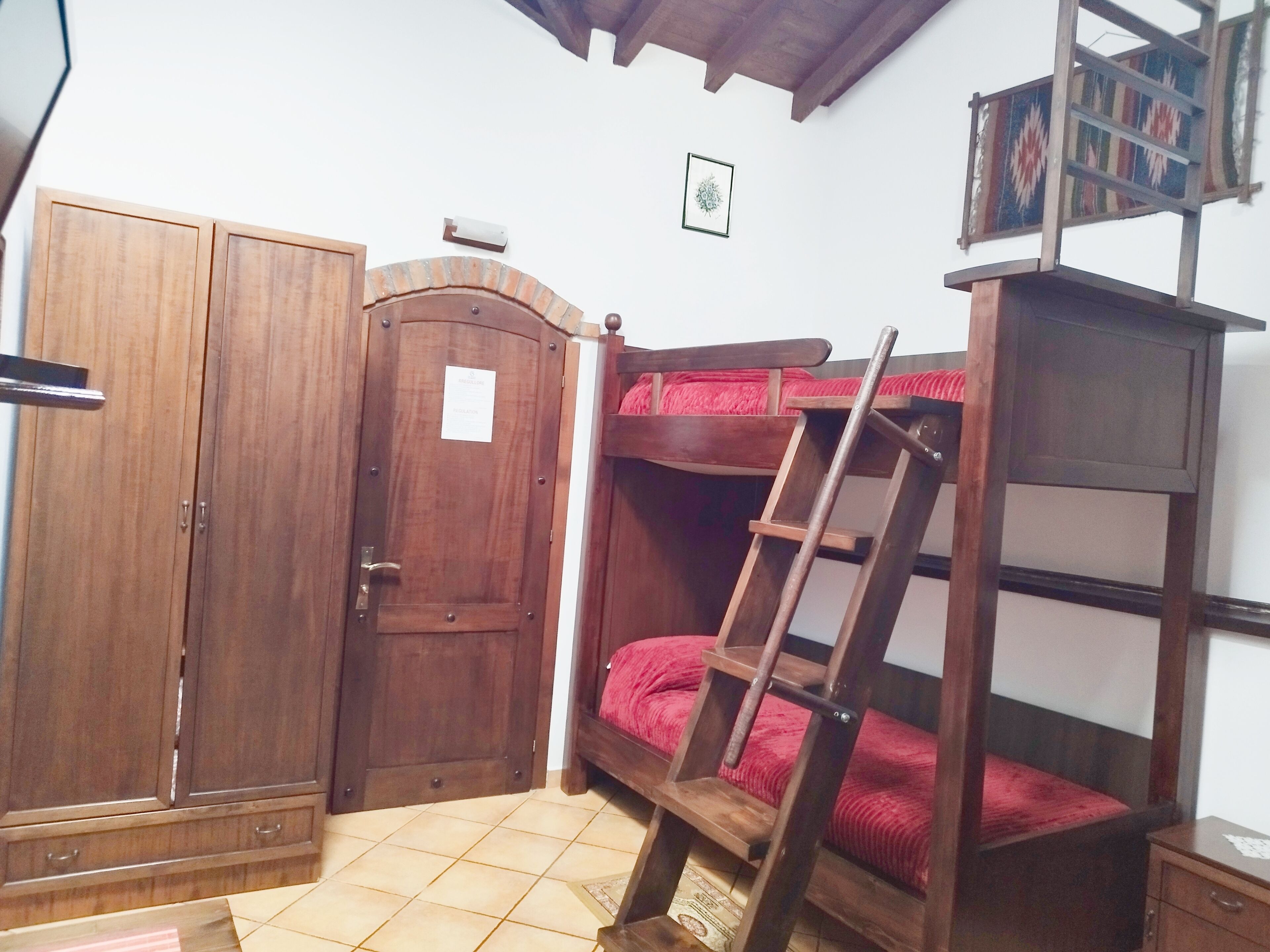 Una habitación con un armario de madera, una cama nido con escalera y una mesita pequeña.