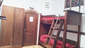 A room with a wooden wardrobe, a bunk bed with a ladder, and a small table.