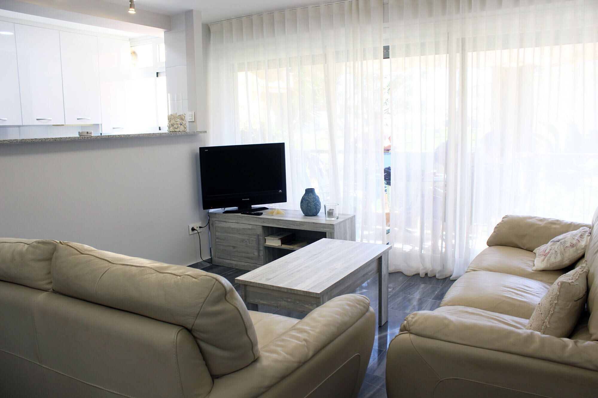 A living room with a beige sofa, a wooden coffee table, a flat-screen TV, and a small side table with a vase and candle.