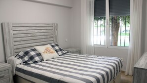 Quarto com colcha listrada, cabeceira de madeira e janela com persianas.