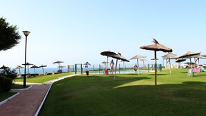 Uma área gramada bem cuidada com piscina, guarda-sóis e vista desimpedida para o mar.