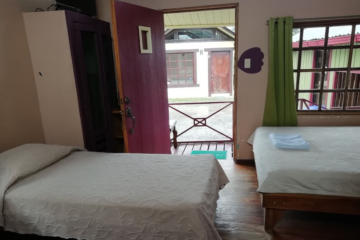 Quarto com duas camas, guarda-roupa de madeira, porta que dá para o exterior e janela com cortinas.