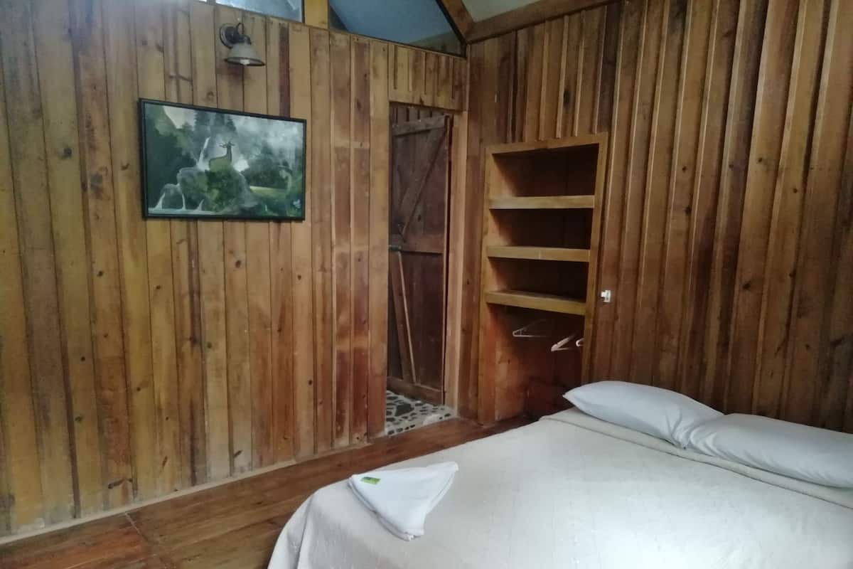 Um quarto de madeira com uma cama, uma estante e uma porta para um banheiro.