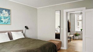 A modern bedroom with a large bed, a bedside table, a mirror, and a view into the adjacent room.