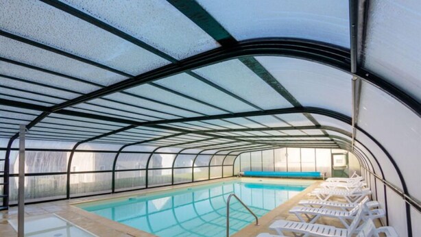 Et overdækket swimmingpool med glasvægge, blåt vand og hvide liggestole.
