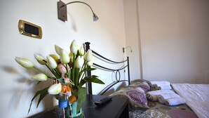A bed with a patterned bedspread, a bedside table with a vase of flowers, a remote control, and a wall-mounted light fixture. - Machiavelli Apartment (lastra a signa)