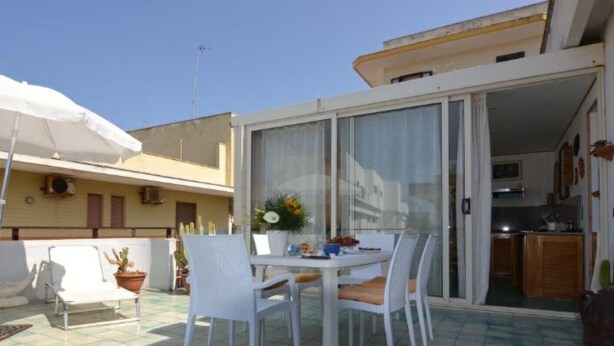 A patio with a table and chairs, a potted plant, and a white umbrella. - Agllipoli Penthouse 215 (Gallipoli)