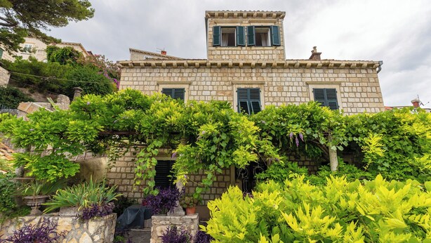 Um edifício de pedra com varanda e um jardim frontal.
