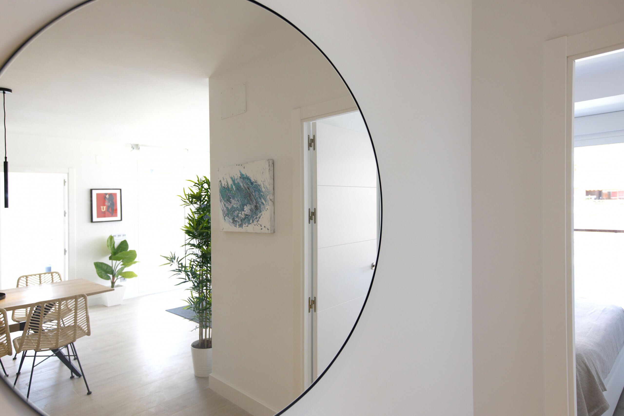 Ein Zimmer mit einem großen Spiegel, der einen Essbereich, einen Blumentopf und eine Tür zu einem weiteren Raum reflektiert.